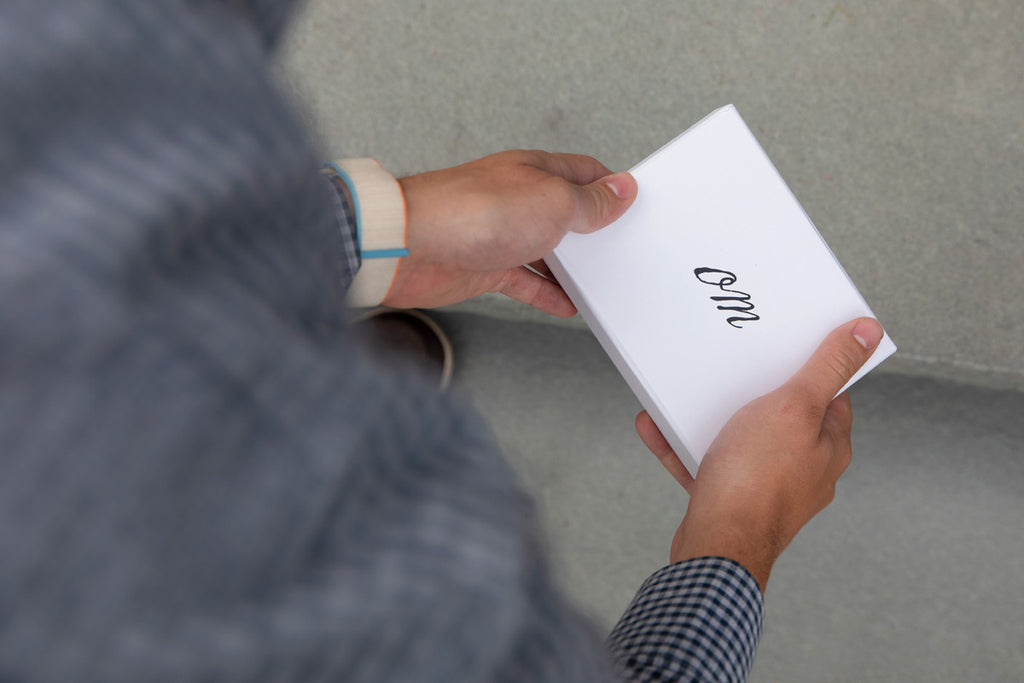 man holding small white box with "OM" in script on top of it