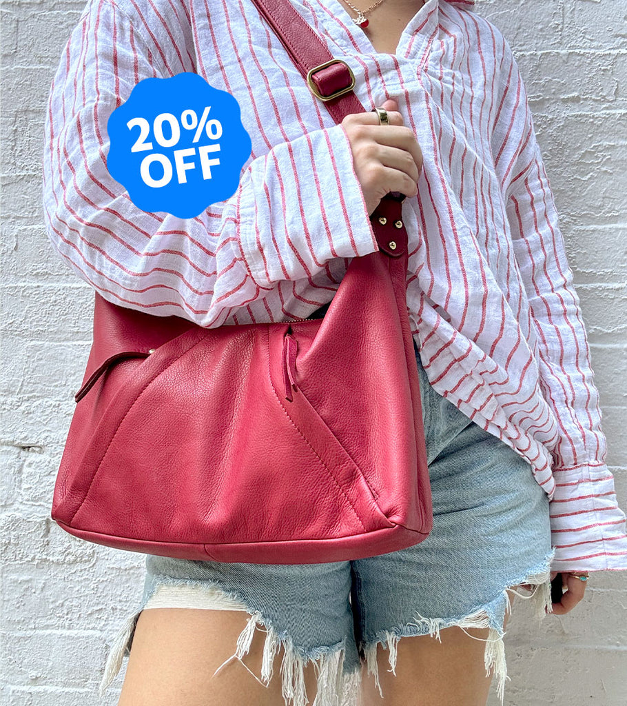 Person holding a red Osgoode Marley handbag with a '20% OFF' label against a light gray brick wall.